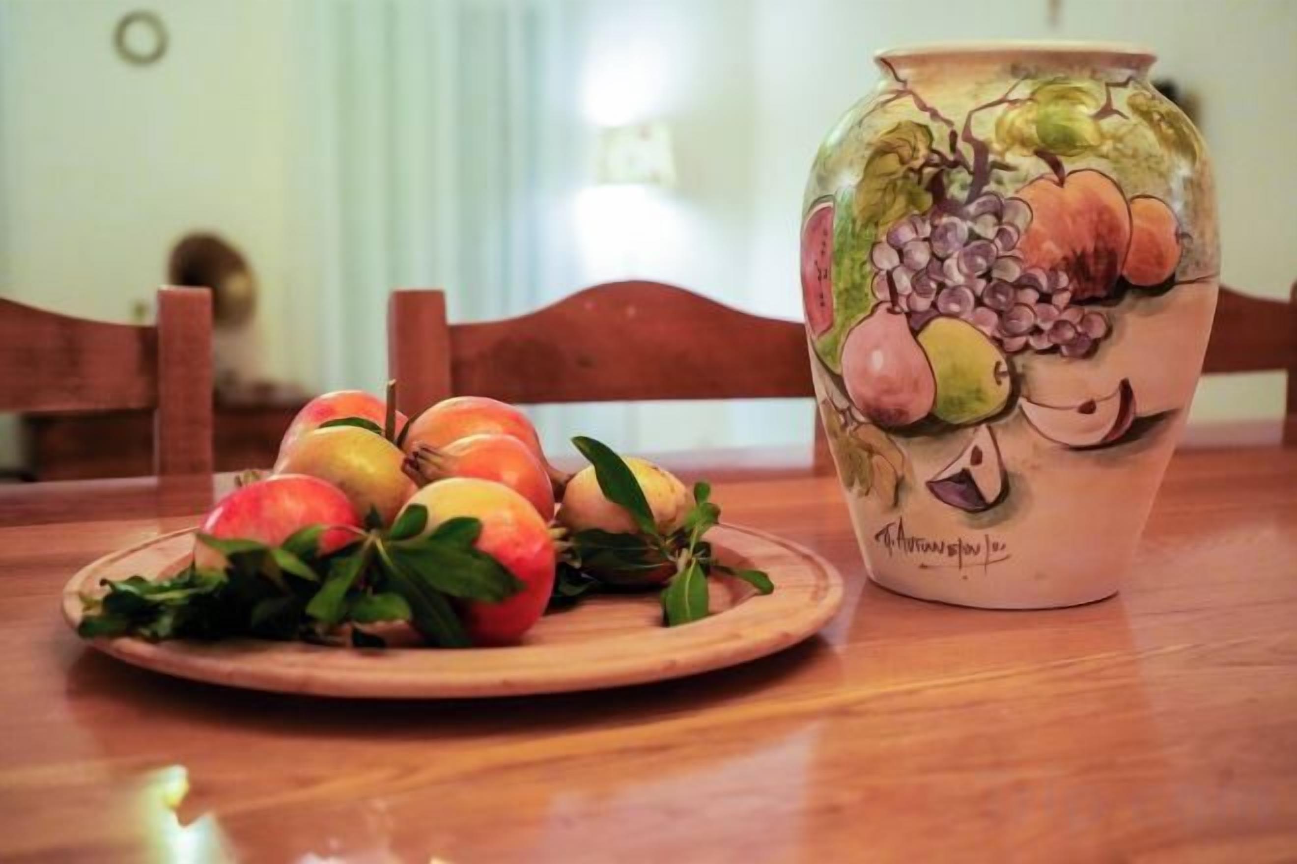 Un tavolo di legno con un piatto di frutta e un vaso in ceramica decorato con motivi di frutta.