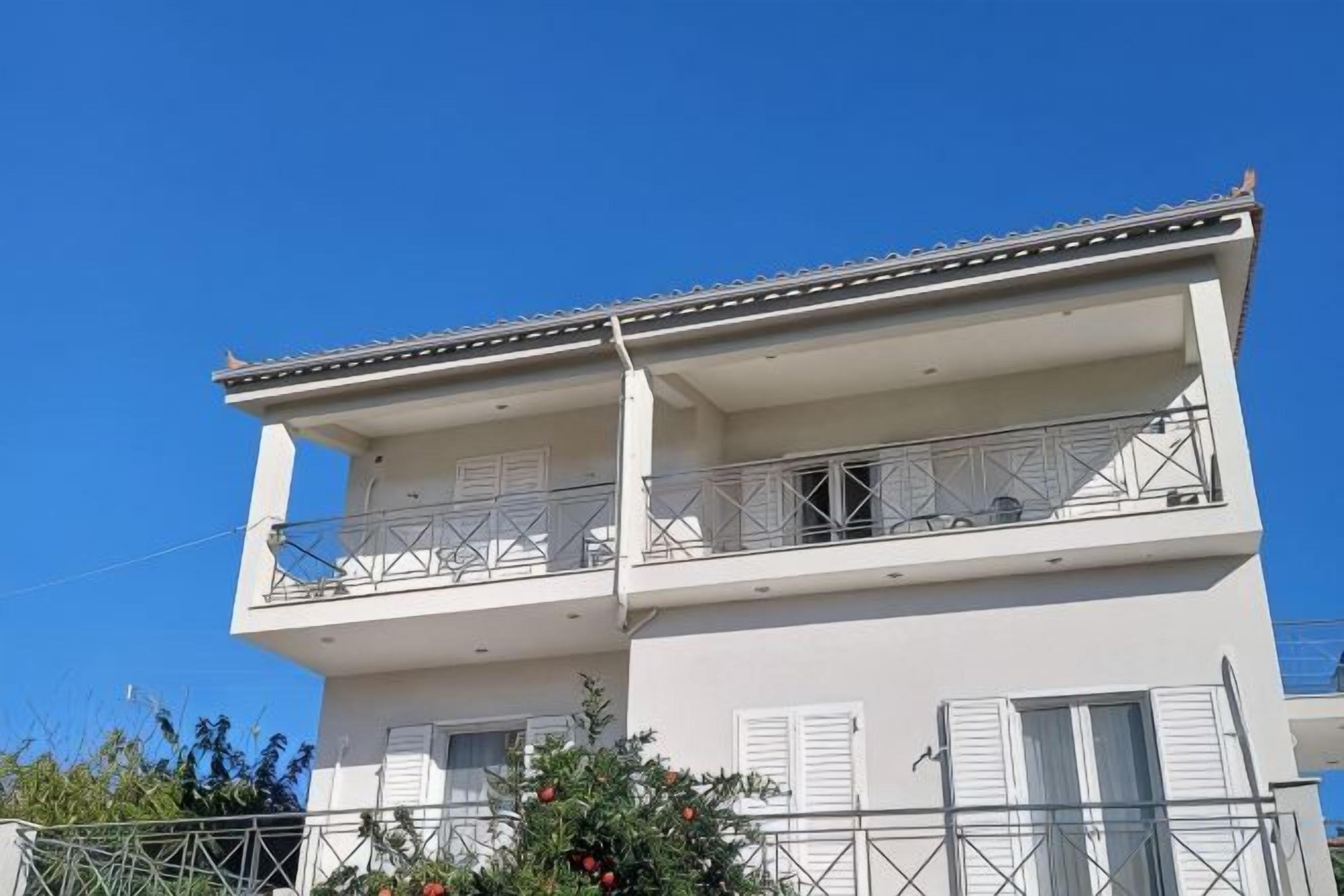A two-story building with a balcony, white exterior, and shutters.