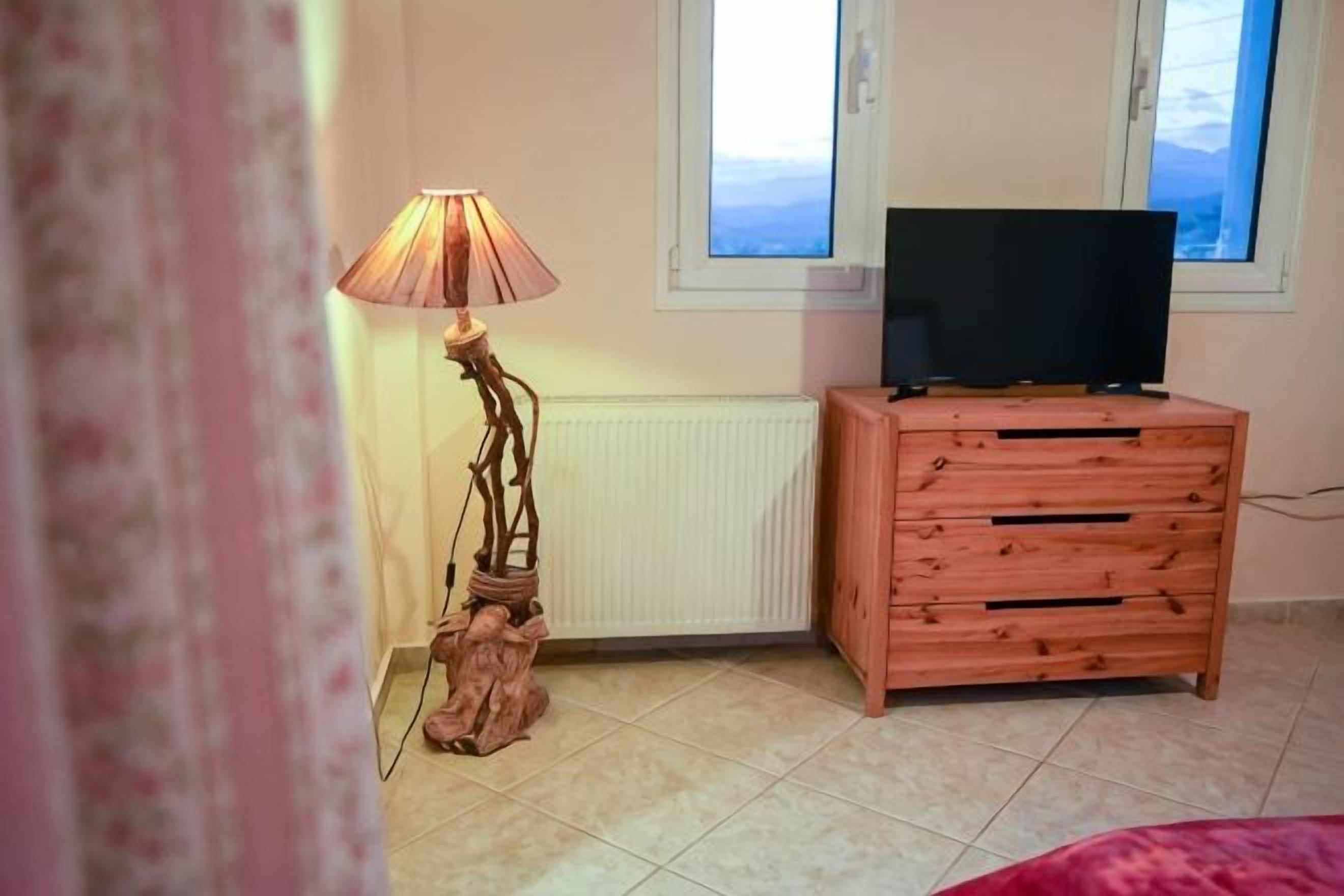 Una stanza con un armadietto in legno, una televisione sopra e una lampada accanto.