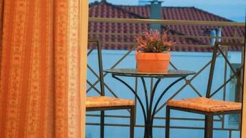 Un balcone con un piccolo tavolo e due sedie, una pianta in vaso, e vista su edifici con tetti rossi.