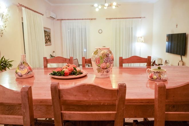 Zona pranzo con tavolo in legno, sedie, un vaso e un piatto di frutta.