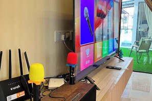 A television with a colorful display, a microphone, and a remote control on a wooden stand. - Happiness Stay (20 Pax) With Karaoke, Snooker, Mahjong Table (Ipoh)