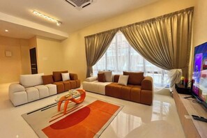 A modern living room with a sectional sofa, a flat-screen TV, and a large window with curtains. - Happiness Stay (20 Pax) With Karaoke, Snooker, Mahjong Table (Ipoh)
