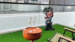 Un balcon avec une petite table sur laquelle sont posés deux coupes à champagne, un panneau d’accueil et une chaise.