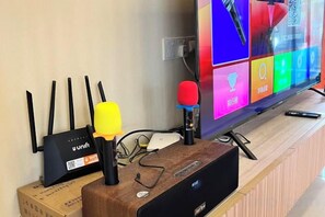A room with a wooden desk, a router, a microphone, and a television displaying colorful icons. - Happiness Stay (20 Pax) With Karaoke, Snooker, Mahjong Table (Ipoh)