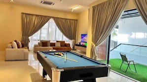 Une table de billard dans un salon, avec deux canapés et un téléviseur.