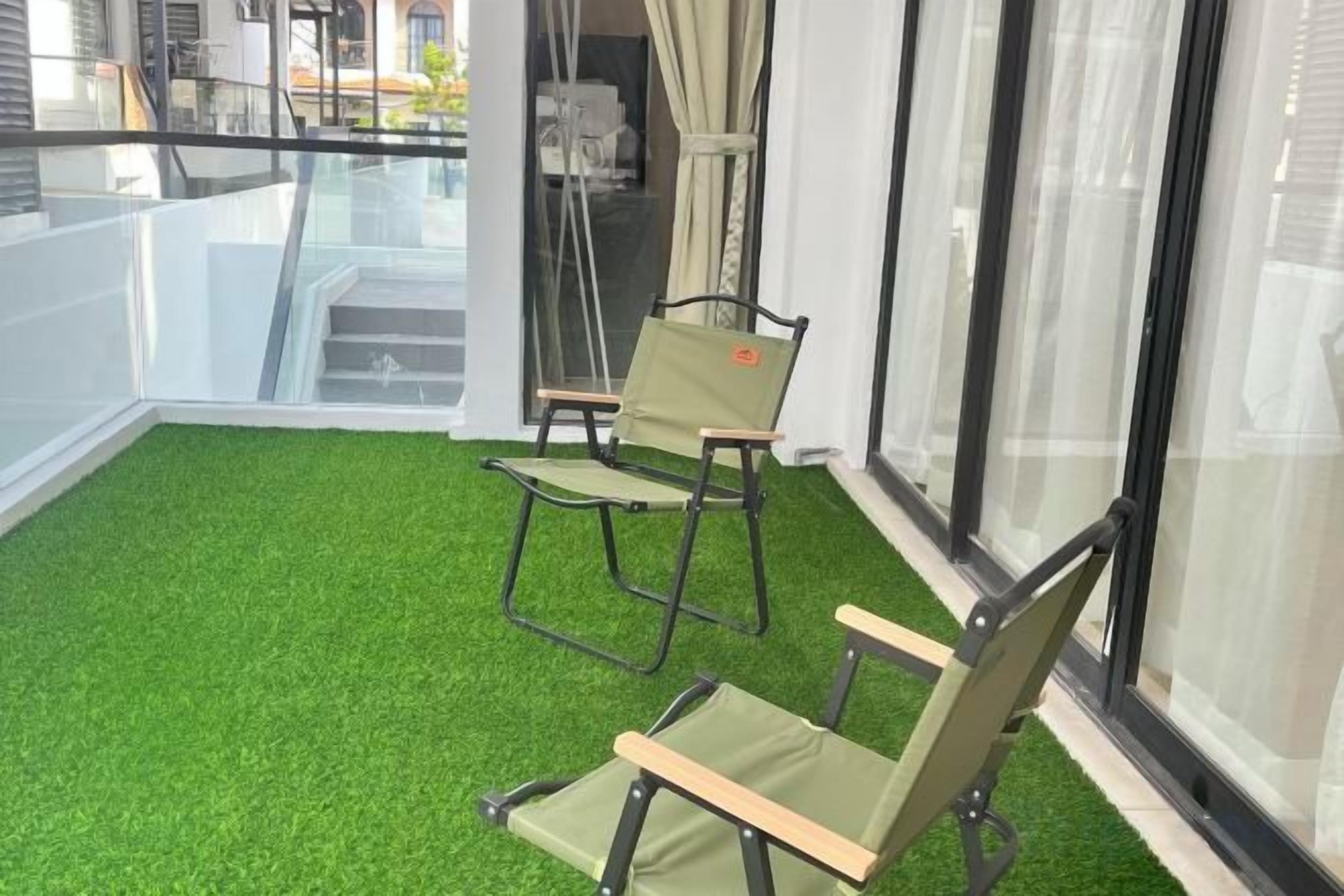 Ein Balkon mit Kunstpflanzen und zwei Stühlen.