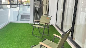 Un balcón con piso verde artificial y dos sillas.
