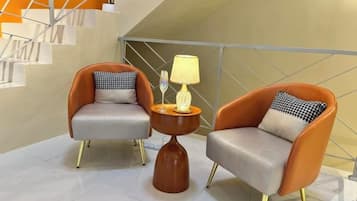 Dos sillones con cojines, una mesita con lámpara y una escalera al fondo.