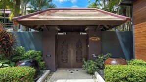 L'ingresso di un edificio con tetto in legno, una porta scura con intagli elaborati e un piccolo giardino con piante in vaso e un vialetto che conduce alla porta.