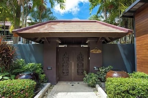 A building entrance with a wooden roof, a dark door with intricate carvings, and a small garden with potted plants and a pathway leading to the door. - Kalim Seaview Boutique Pool Villa (Phuket)