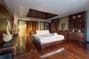 Un dormitorio espacioso con una cama grande, suelo de madera y estanterías empotradas decoradas con objetos ornamentales.