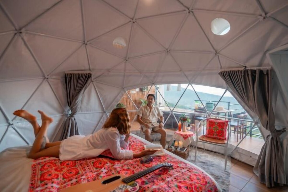 A tented accommodation with a bed, a table, and a view of the outdoors.