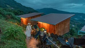 A wooden cabin with a sloped roof, surrounded by lush greenery and mountains in the background. - Mon Sa Kiang Dao (Mae Rim)