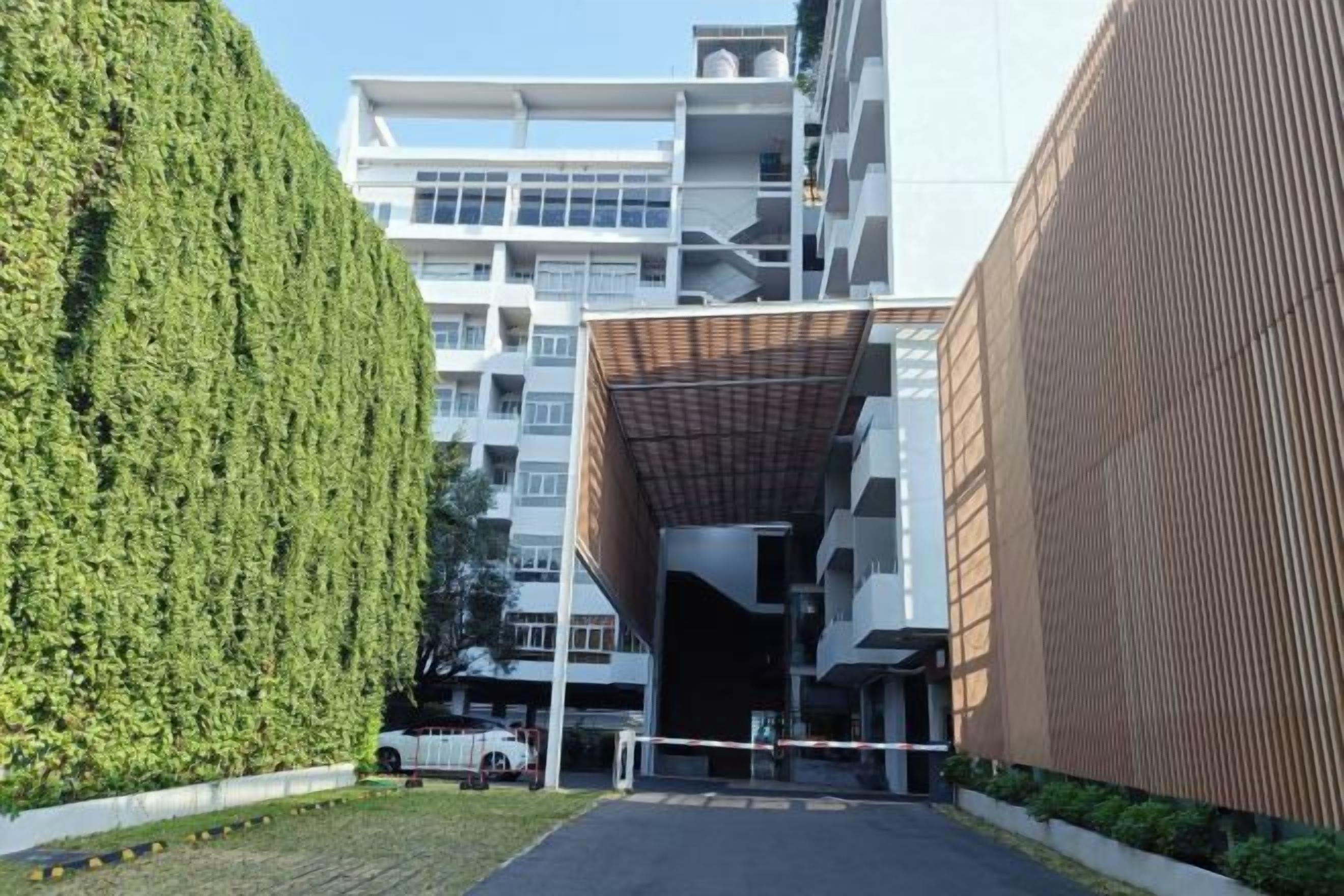 A modern building with a covered entrance, a green hedge, and a white van parked in front.