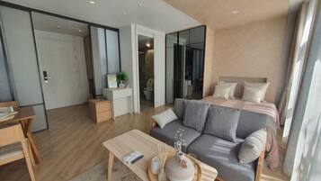 A modern hotel room with a sofa, a coffee table, a bedside table, and a large window.