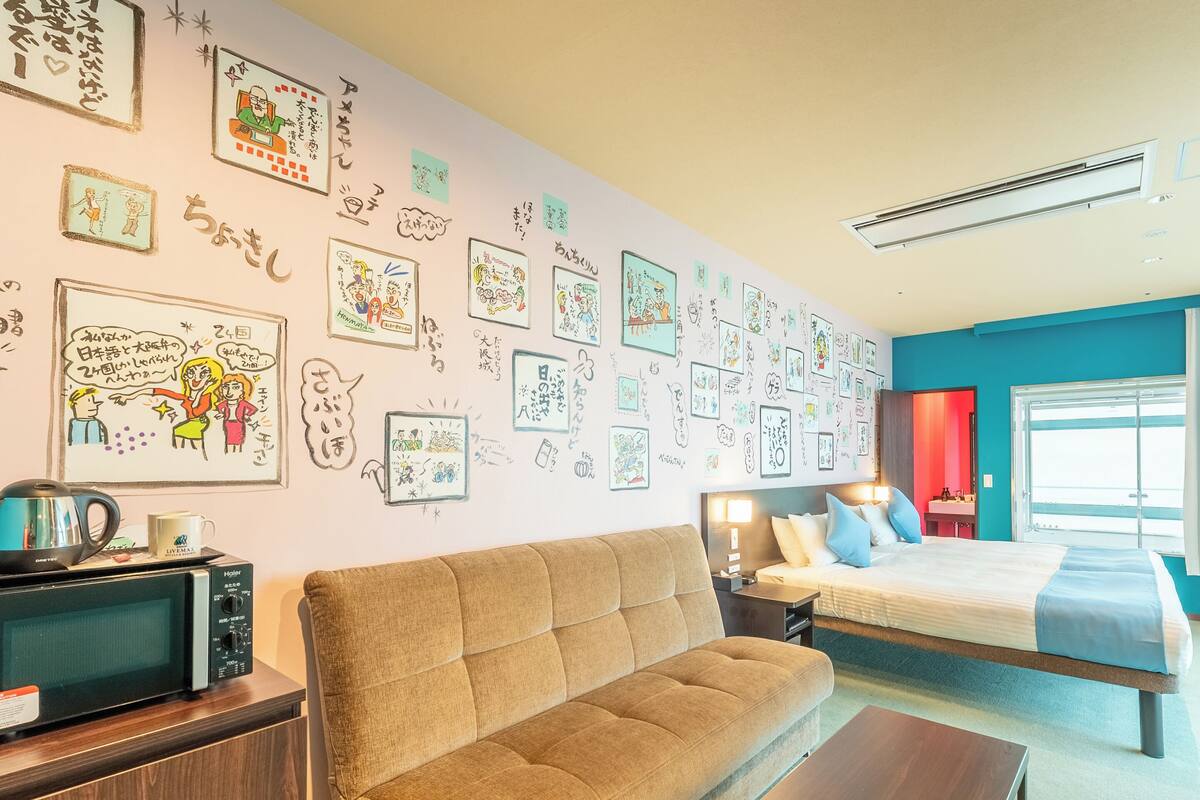 A hotel room with a sofa, a bed, a coffee table, and a wall decorated with various drawings and writings.