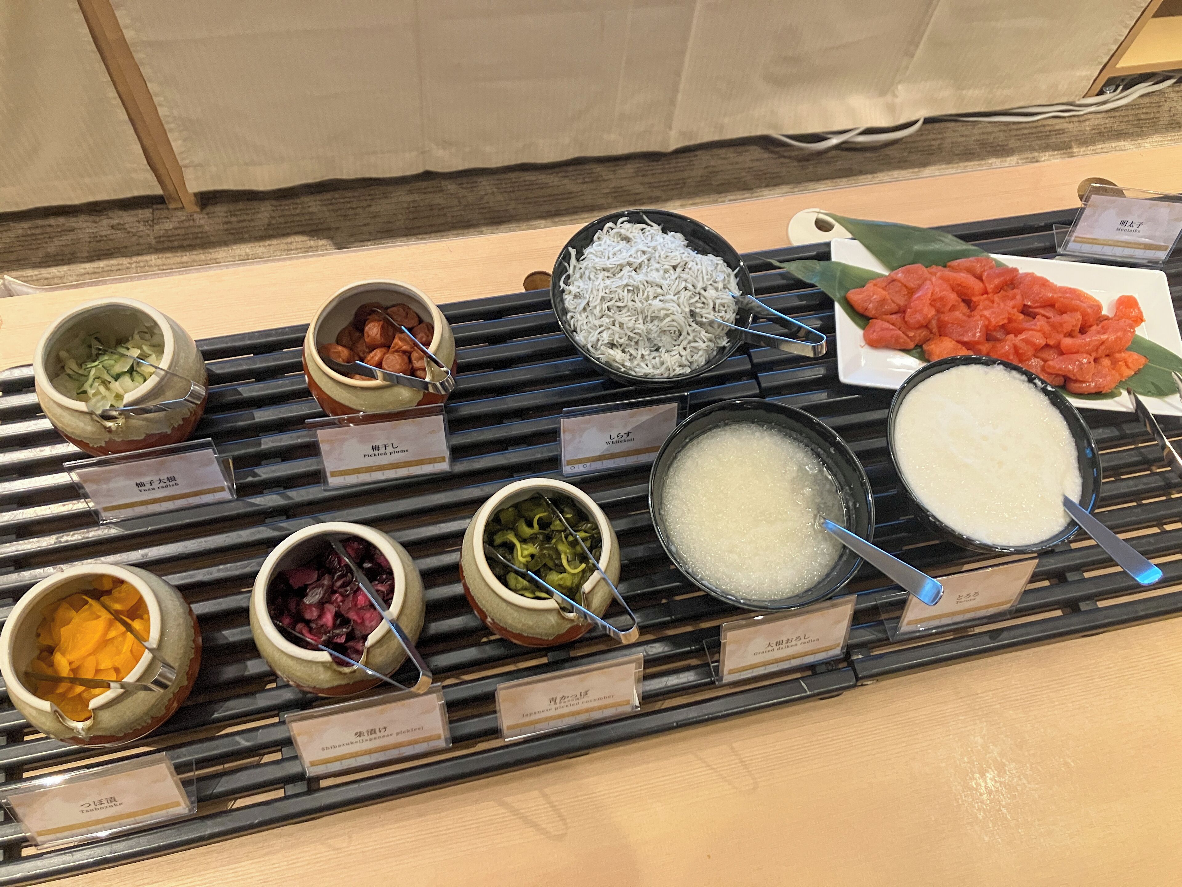 A buffet with various dishes including pickled vegetables, a bowl of rice, and a plate of sliced meat.