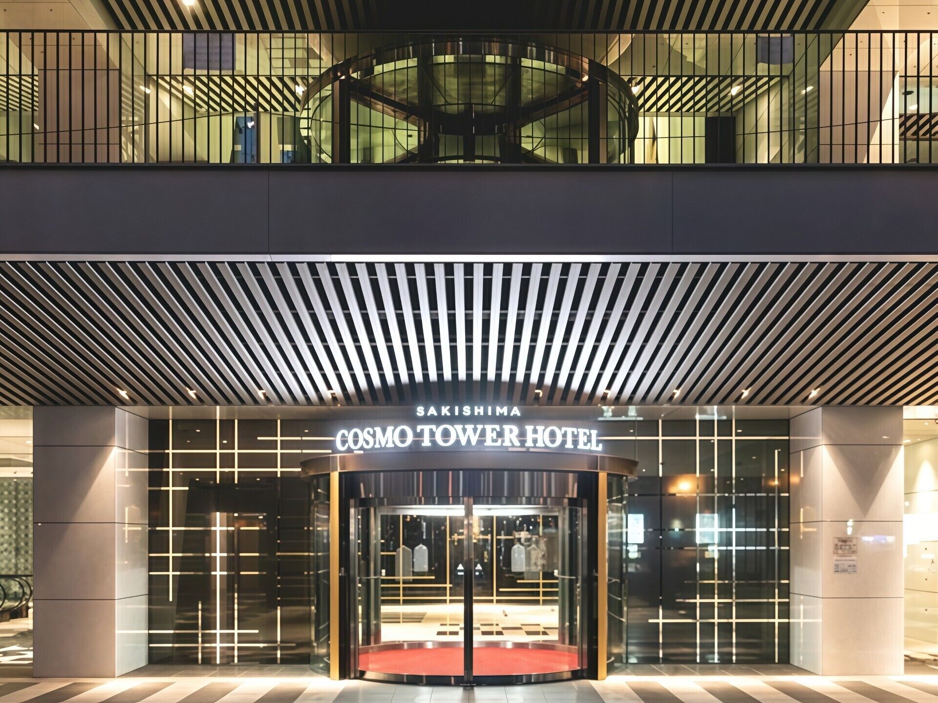 Indgangen til Cosmos Tower Hotel med et moderne design, der inkluderer en roterende dør og en glasfacade.