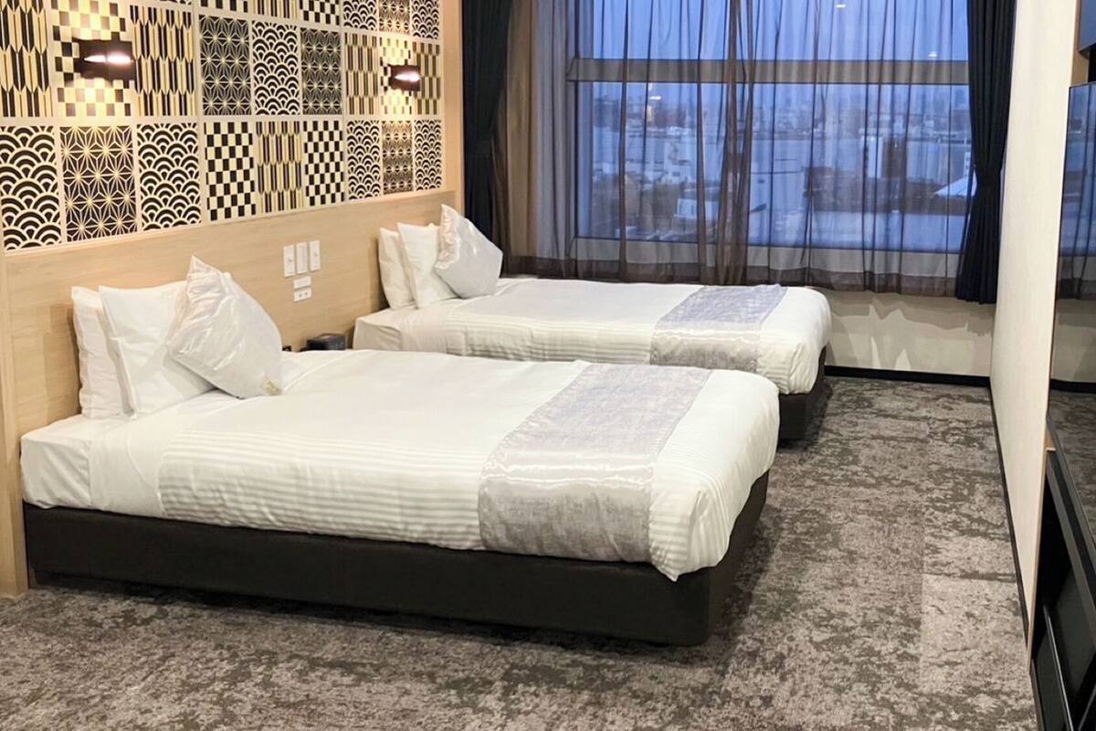 A hotel room with two beds, a patterned wall, and a large window with a view.
