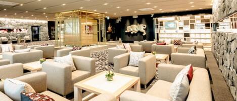 A modern lounge area with sofas and tables, a stone wall, and a decorative wall with framed pictures.