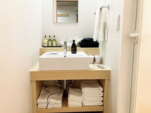 A bathroom with a white sink, mirror, and towel rack. There are toiletries on the counter and towels in a cabinet below. - LiVEMAX Sakishima Cosmo Tower Hotel (Osaka)