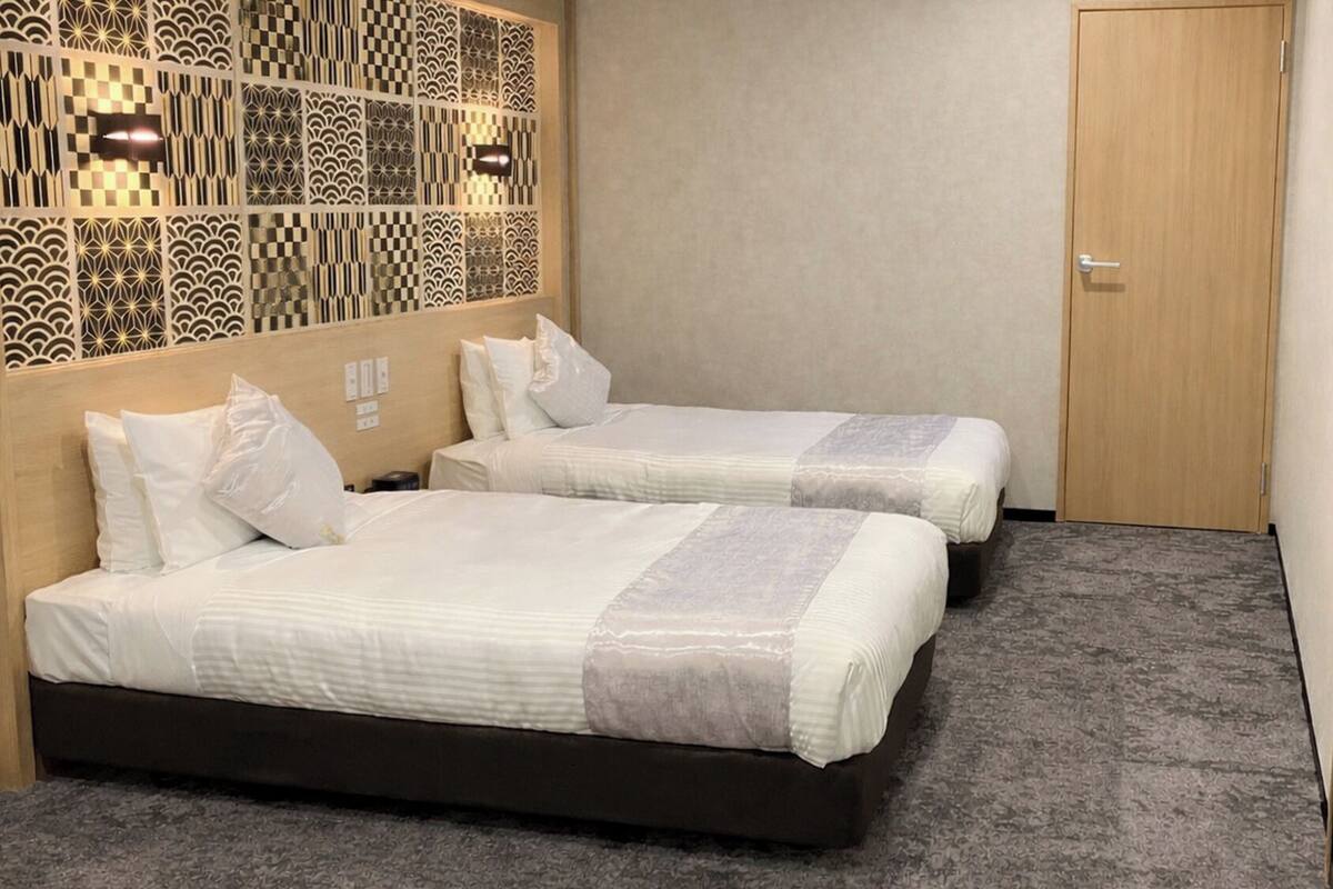 A hotel room with two beds, a patterned headboard, a wooden door, and a carpeted floor.
