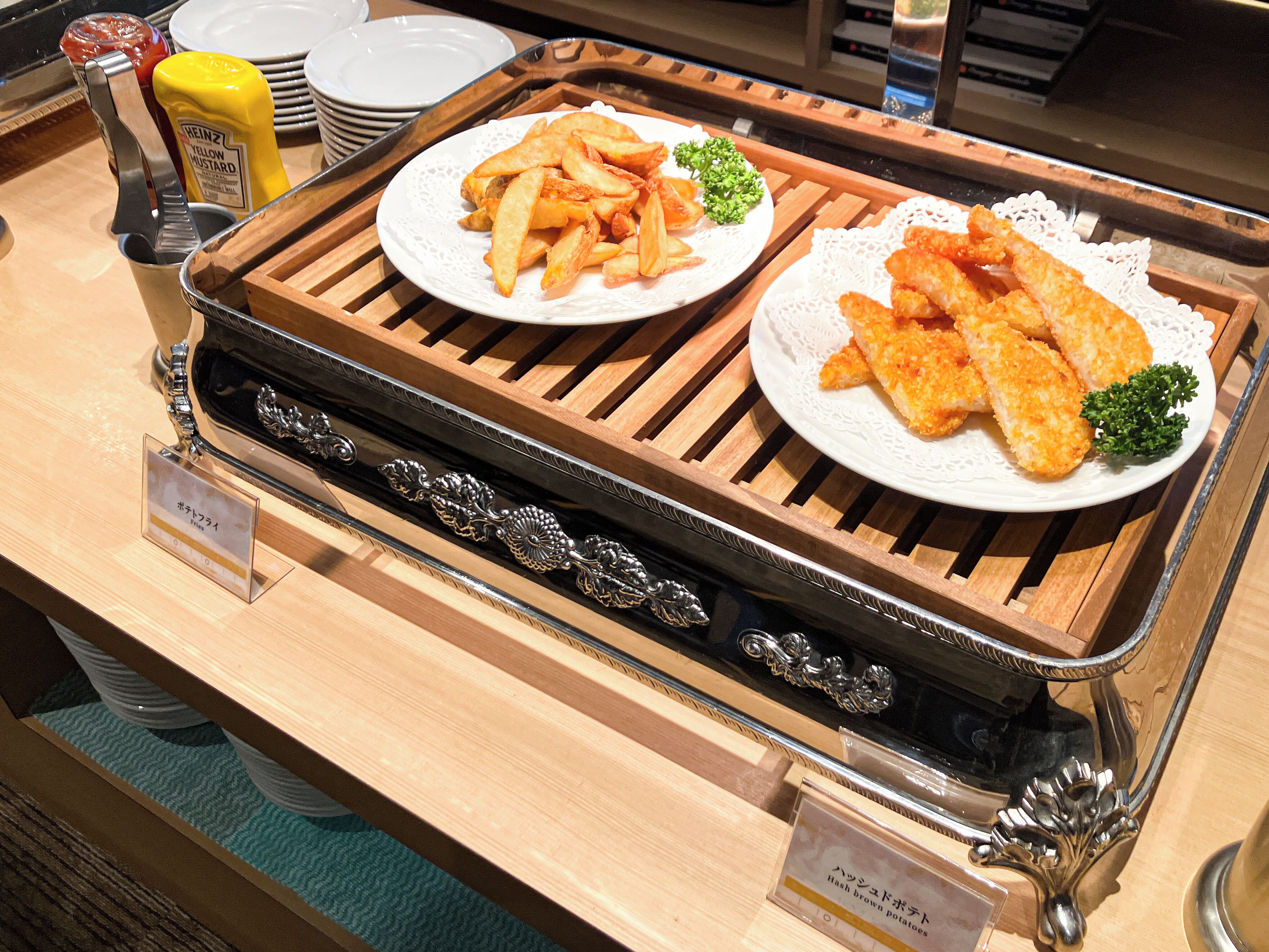 Una mesa de buffet con platos de papas fritas y pescado, botellas de mostaza y kétchup.
