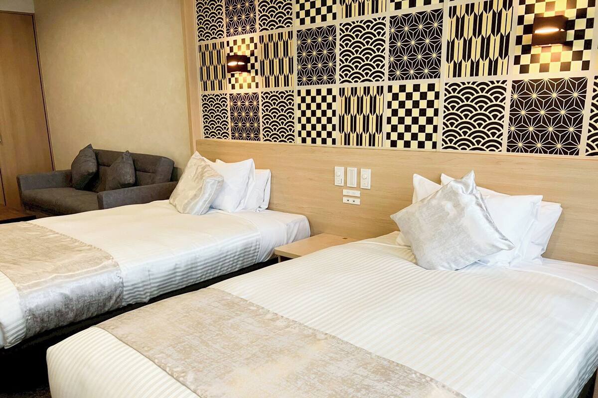 A hotel room with two beds, a sofa, and a decorative wall panel.