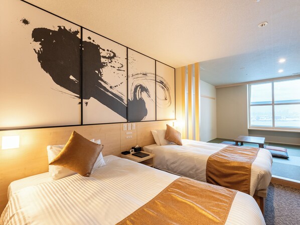 A hotel room with two beds, a large abstract painting on the wall, a window with a city view, and a small table.