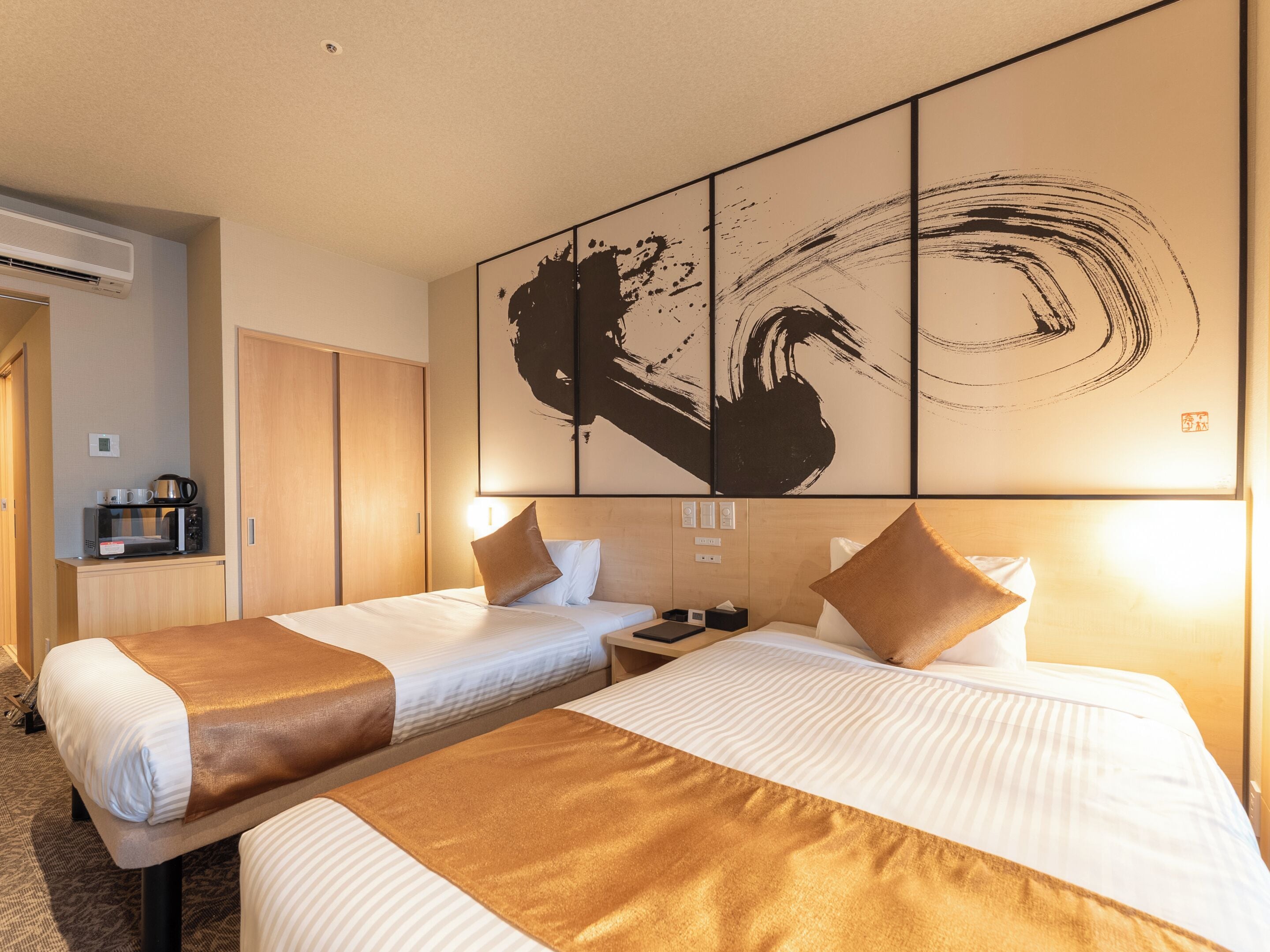 A hotel room with two beds, a minibar, a coffee machine, and a large abstract painting on the wall.