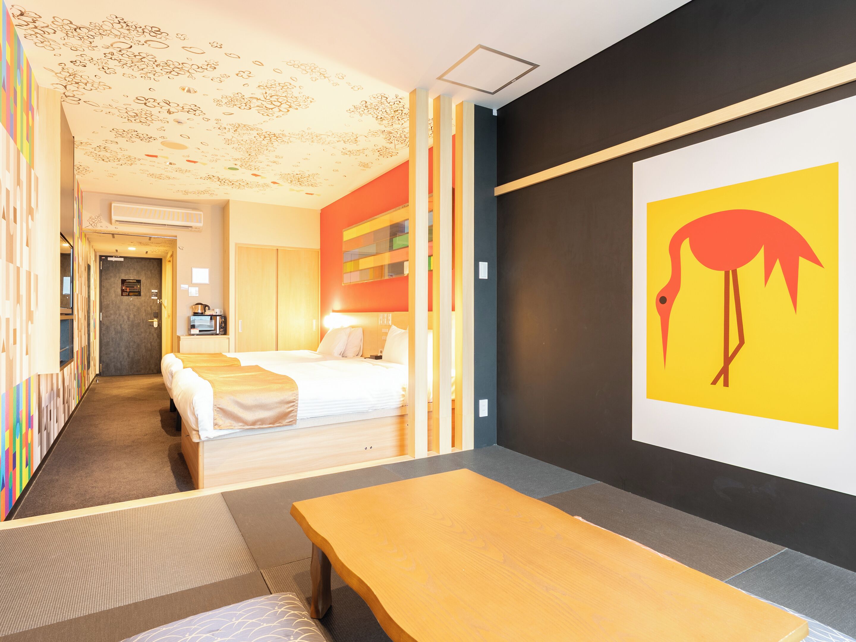 A hotel room with a bed, a desk, and a wall with a colorful painting.