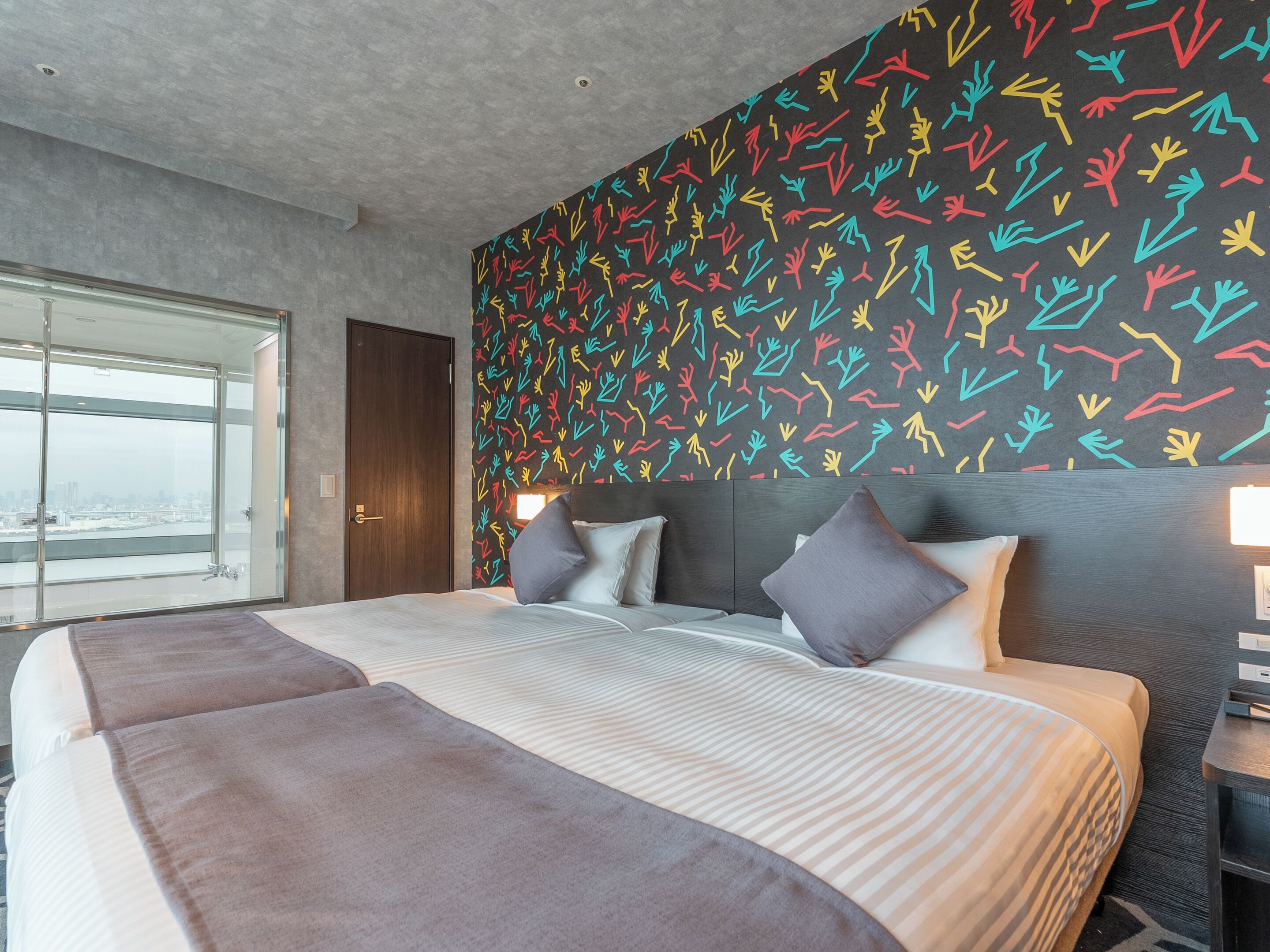 A modern hotel room with a large bed, two bedside tables, and a city view.