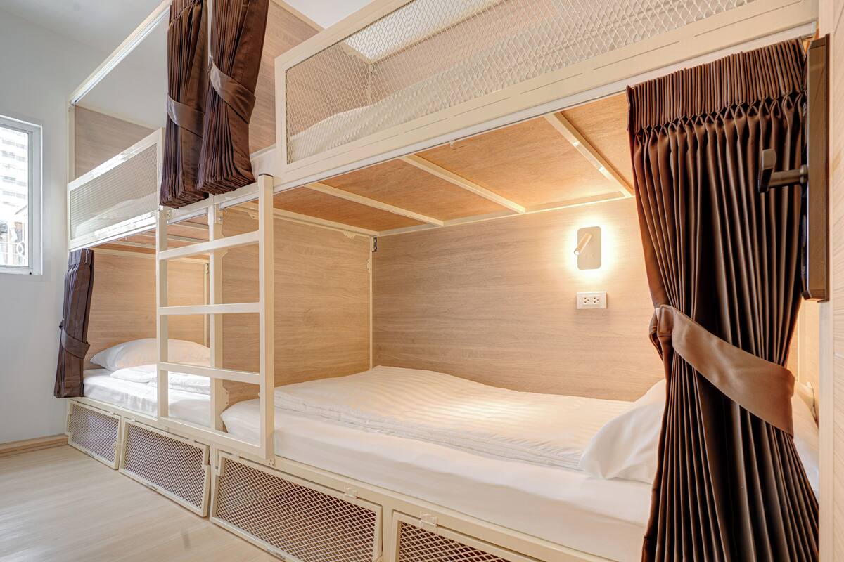 Une chambre avec un lit superposé, une fenêtre, des rideaux et une lampe fixée au mur.