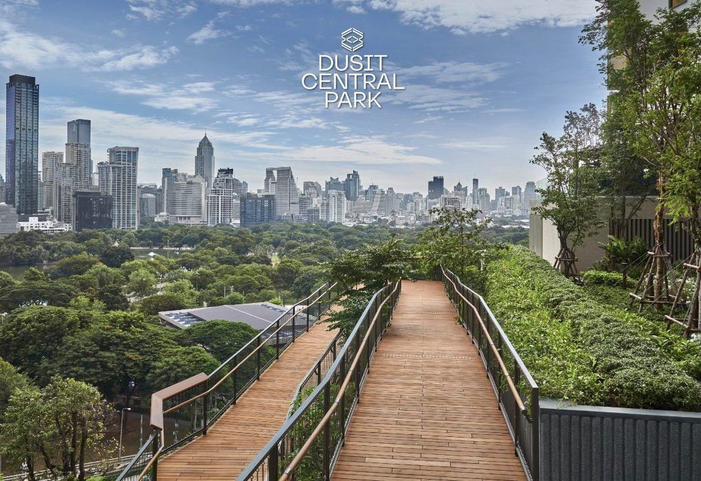 A wooden boardwalk leading through a park with a city skyline in the background.
