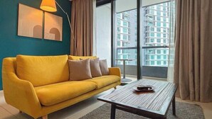 Ein Zimmer mit einem gelben Sofa, einem Holztisch, einer Stehlampe und einem großen Fenster mit Blick auf ein Gebäude.
