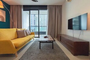A modern living room with a yellow sofa, a coffee table, a flat-screen TV, and a view of high-rise buildings through the window. - Nostalgia Arcoris #163 #Hyatt #MontKiara (Kuala Lumpur)