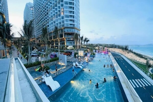 Zona de piscina con tobogán de agua, junto a una playa y un edificio de gran altura.
