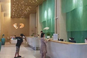 Un área de recepción con mostrador, una planta y un muro con arte abstracto.