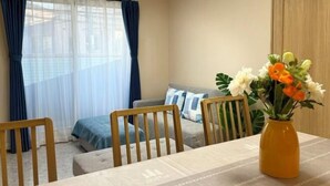 A room with a dining table, chairs, a sofa, and a vase with flowers. - Lapis House 201-2F (Tokyo)