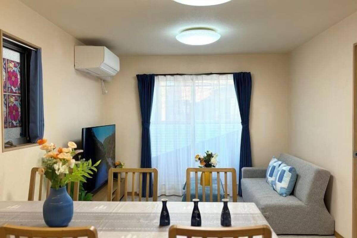 A small room with a dining table, chairs, a sofa, a TV, and a window with curtains.