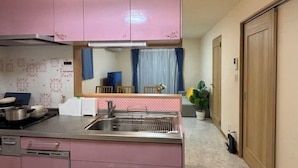 A kitchen with pink cabinets, a stainless steel sink, and a window with blue curtains. - Lapis House 201-2F (Tokyo)