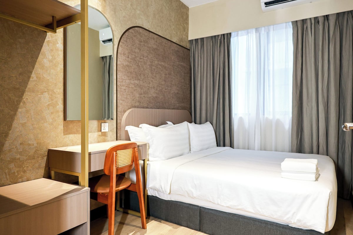 Une chambre d’hôtel avec un lit, un bureau, une chaise et un grand miroir.