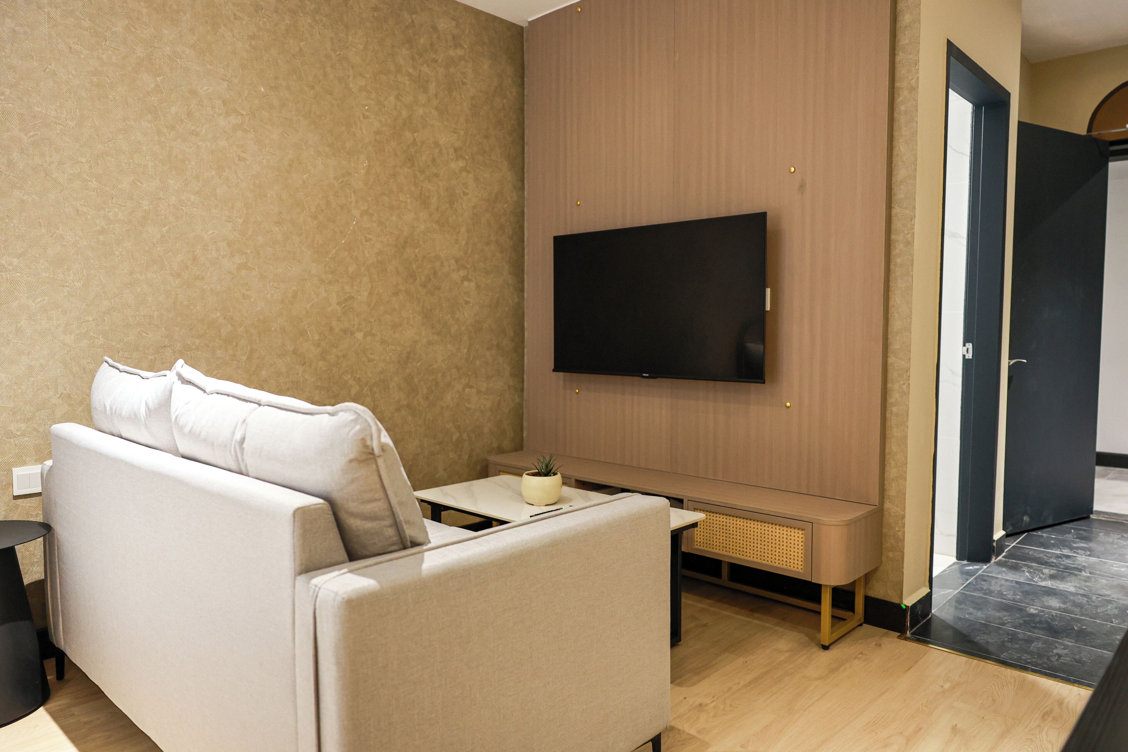 A modern living room with a sofa, a flat-screen TV, a small table, and a potted plant.