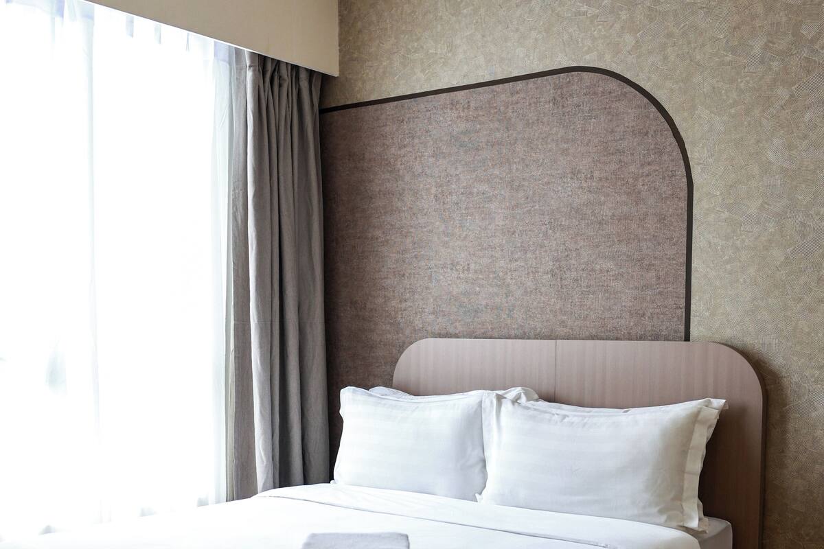 Un lit bien fait, avec du linge de lit blanc et des oreillers, une tête de lit sombre et un plancher en bois.