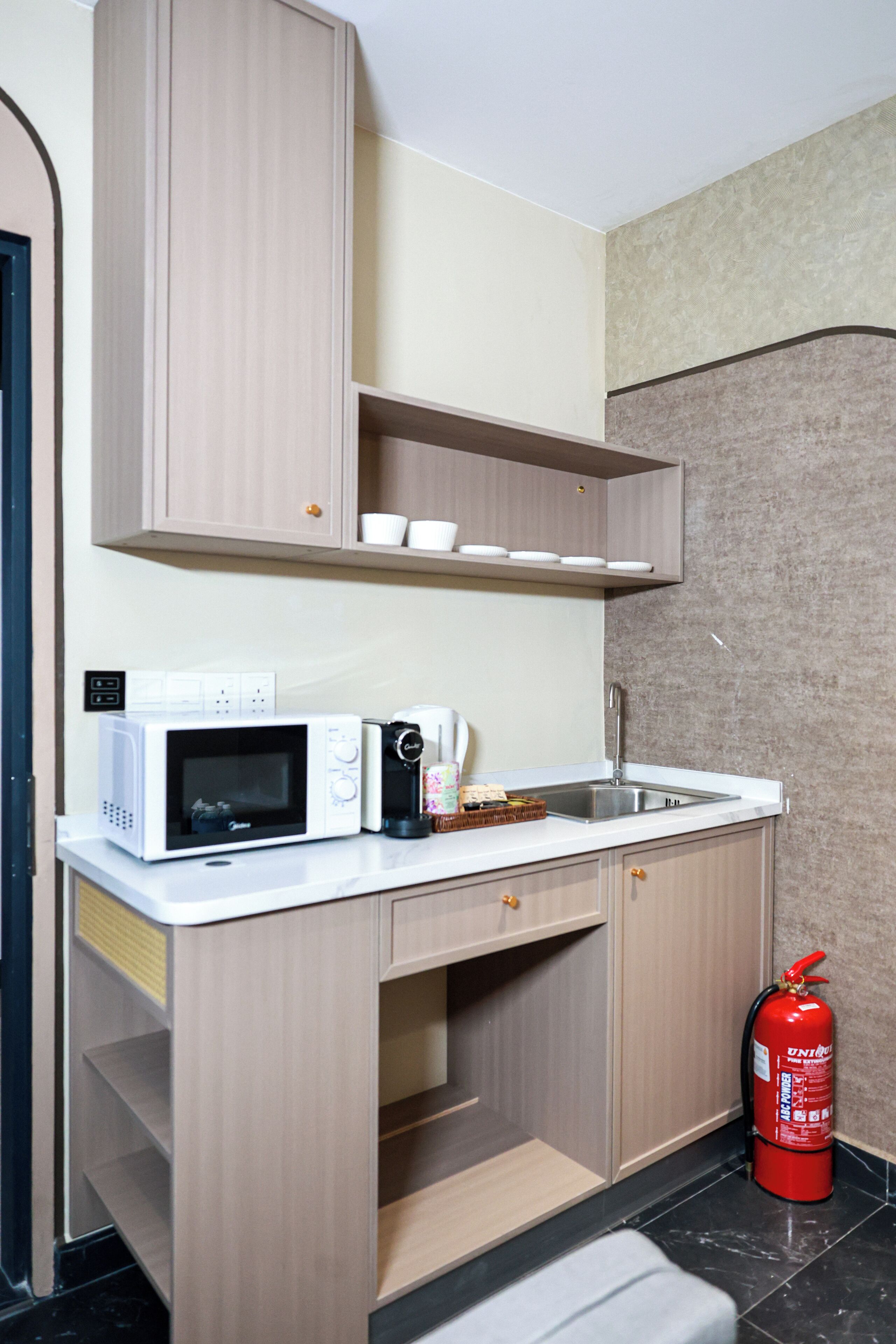 Cocina compacta con microondas, cafetera y extintor.