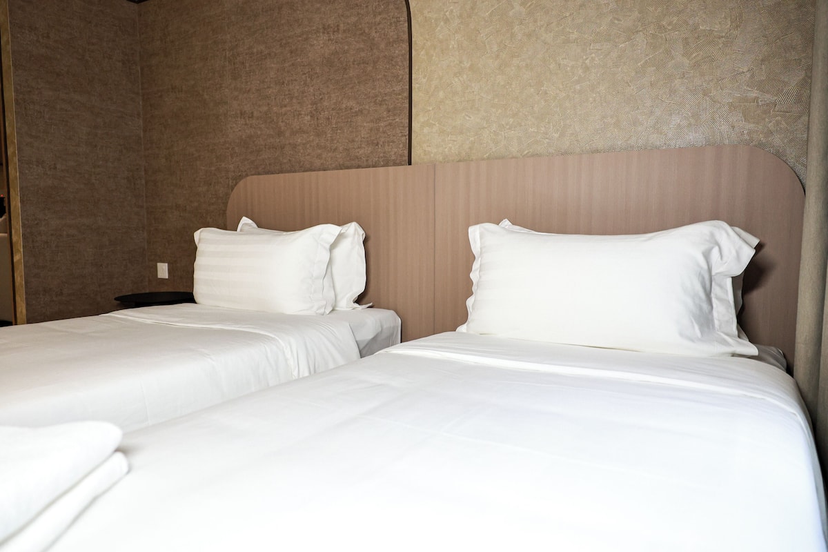 Une chambre d’hôtel avec deux lits, chacun étant équipé de draps et d’oreillers blancs.