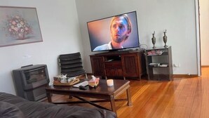 A living room with a flat-screen TV, a fireplace, a coffee table, and a bookshelf. - 3 Bed room Villa 19 Mins to Melbourne center (Laverton)