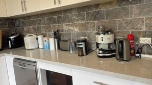 A kitchen with a stone backsplash, various appliances, and a coffee maker. - 3 Bed room Villa 19 Mins to Melbourne center (Laverton)