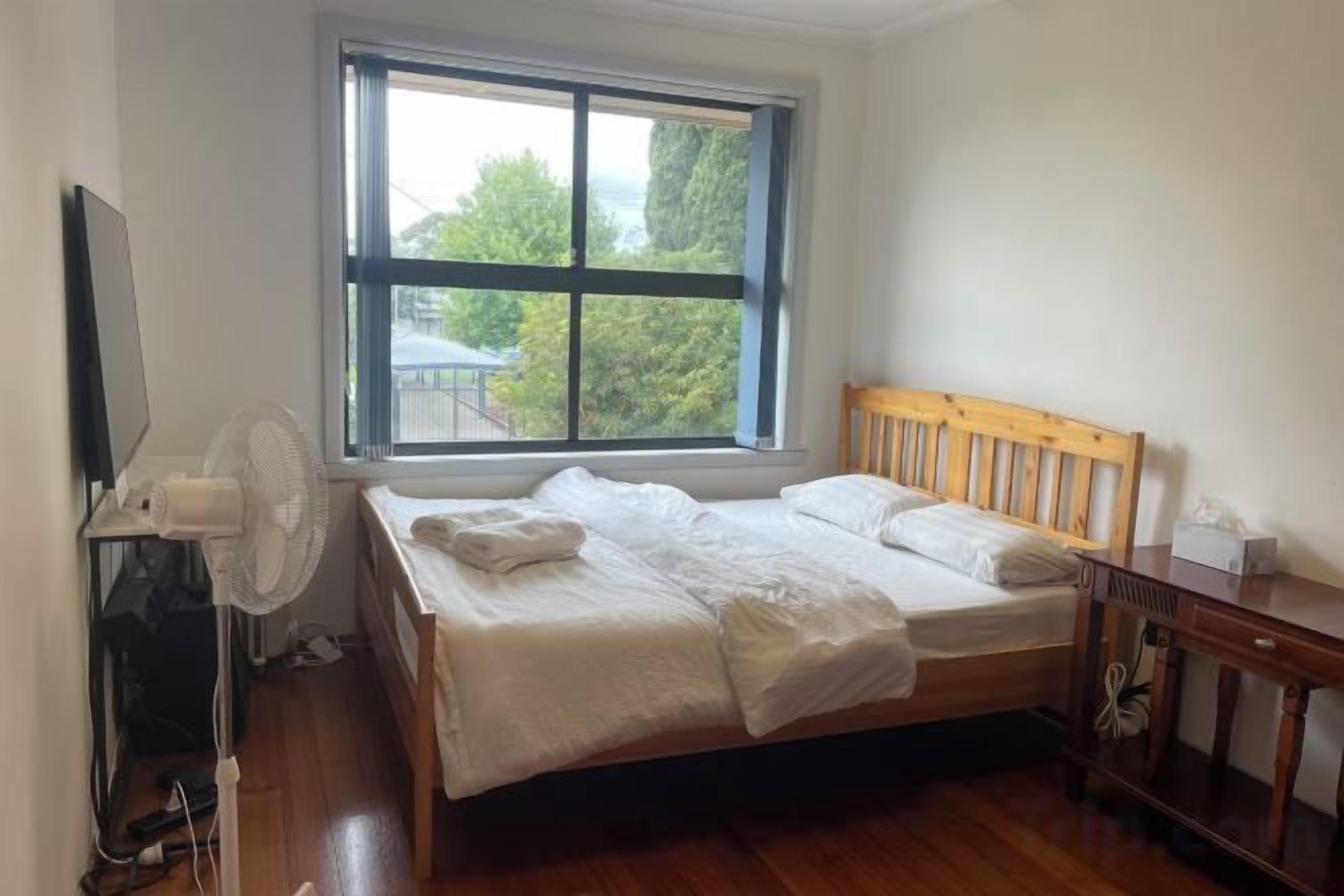 A bedroom with a bed, a wooden headboard, a window, a desk, and a chair.